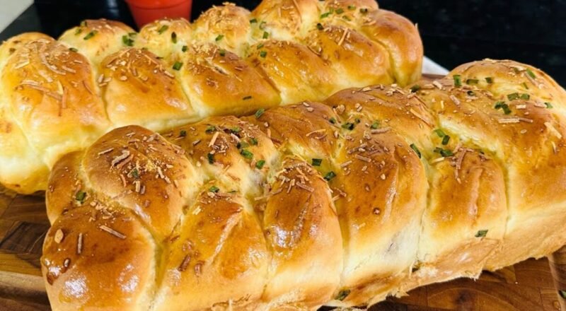 Trança de calabresa assada, dourada e com queijo por cima, em uma mesa de madeira