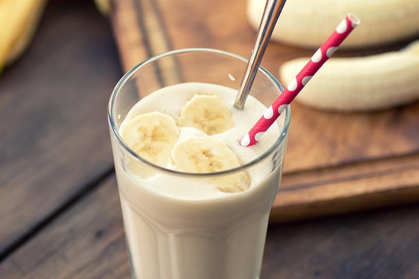 Smoothie de banana cremoso em um copo com ingredientes ao fundo